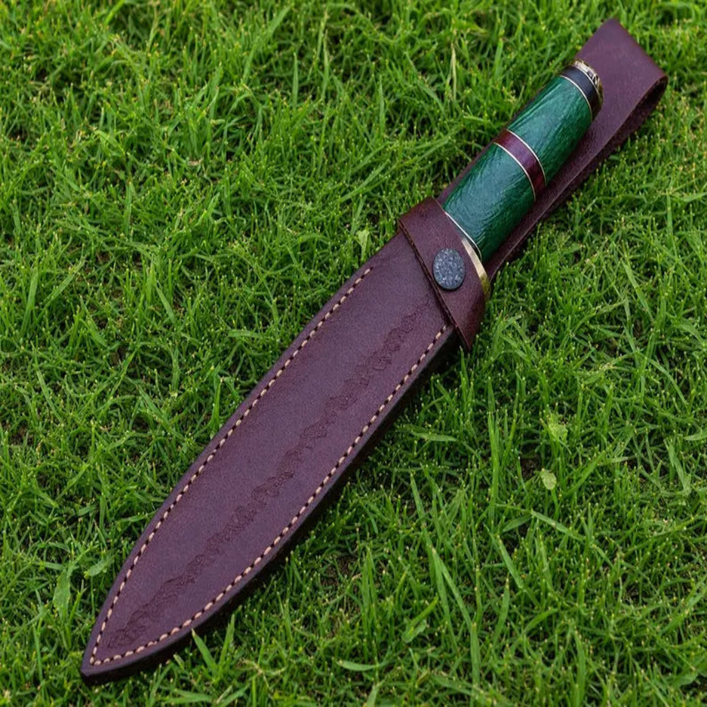 A fixed-blade knife with a green inlay handle and a dark brown leather sheath, displayed diagonally on a green grass background.