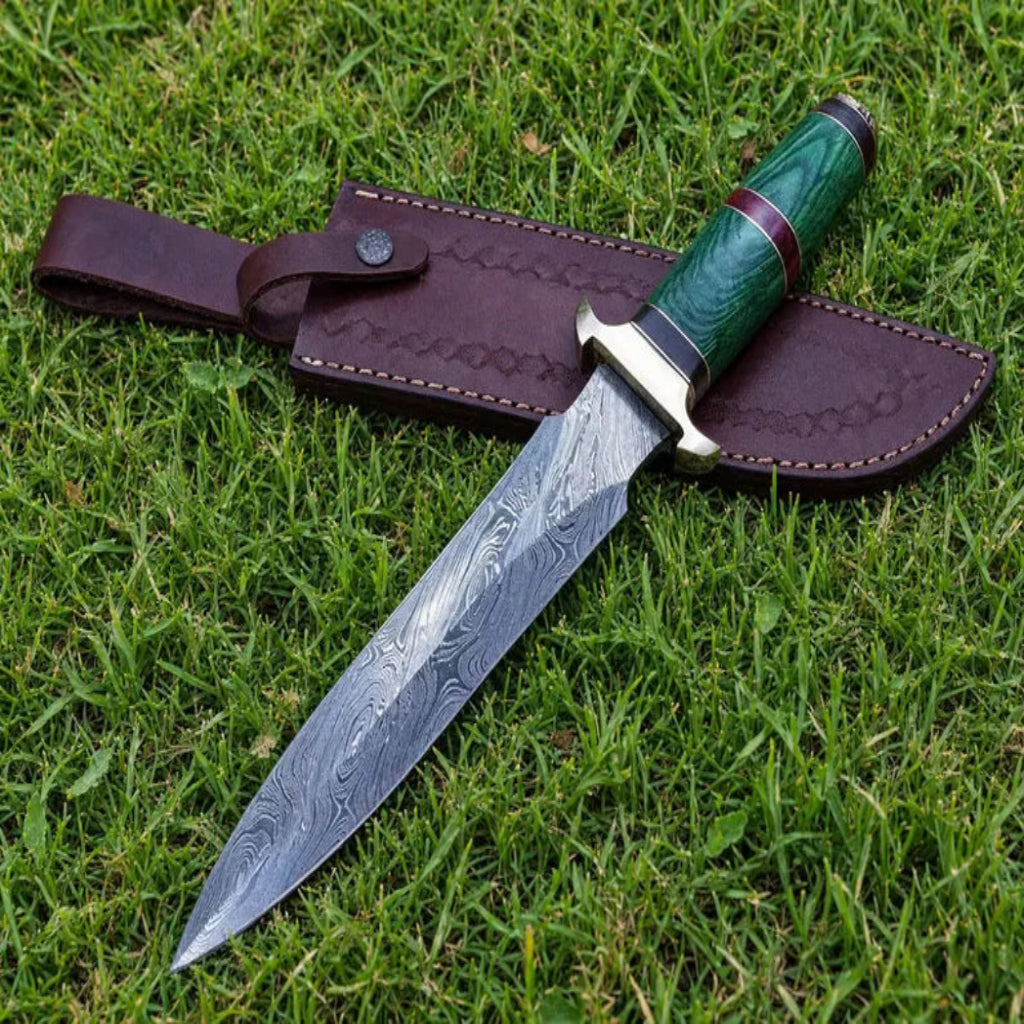A fixed-blade knife with a patterned steel blade, green handle, and brown leather sheath, placed on green grass.